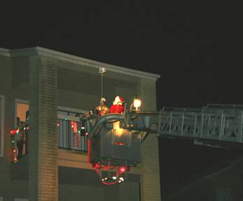 Santa Claus being lifted to rooftop by fire truck ladder